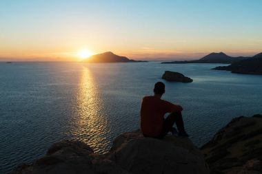 Adam silüeti kayalıklarla ve deniz üzerinde gün batımını izlemek.