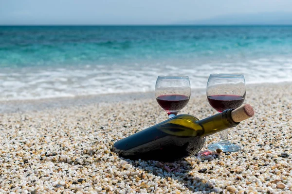 Glasses of red wine and bottle on the beach at the summer sunny day