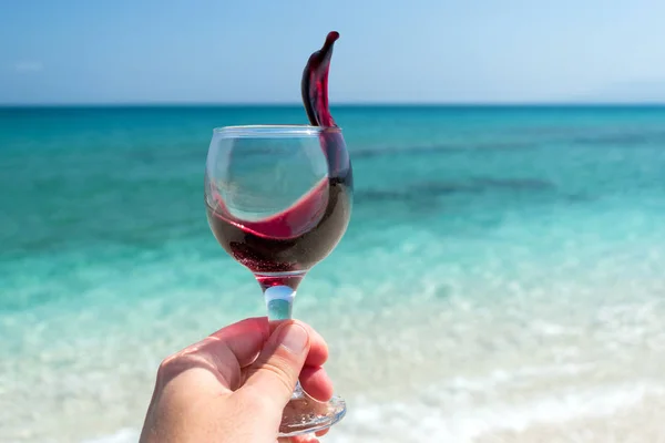 Hand met glas rode wijn op het strand bij het zonnige zomerdag — Stockfoto