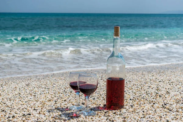 Glasses of red wine and bottle on the beach at the summer sunny day