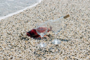 Bir şişe kırmızı şarap yaz güneşli gün plajda şarap bardakları ile. Deniz arka planda.