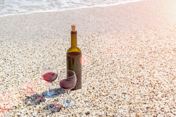 Glazen rode wijn en een fles op het strand bij het zonnige zomerdag — Stockfoto