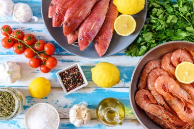 Taze karides ve otlar ve baharatlar ile mavi ahşap arka plan üzerinde kırmızı Kefal balık.