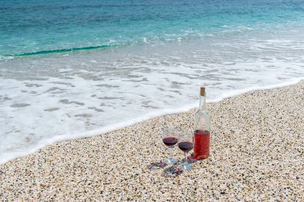 Glasses of red wine and bottle on the beach at the summer sunny day. Sea on the background.