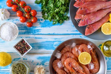 Taze karides ve otlar ve baharatlar ile mavi ahşap arka plan üzerinde kırmızı Kefal balık. Düz yatıyordu.