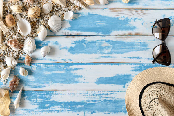 Seashells on blue wooden board with straw hat and sunglasses. Summer holiday background.