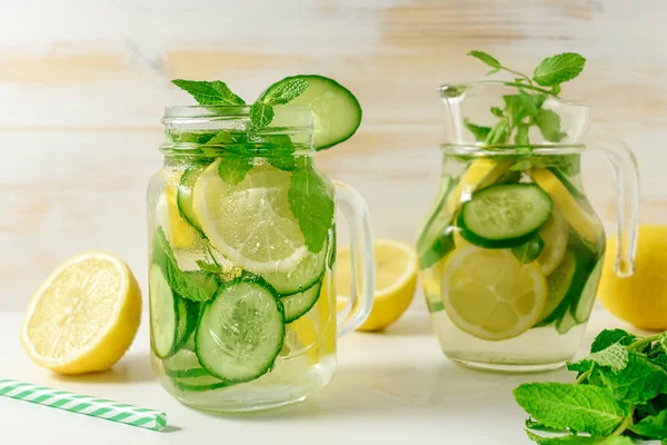 Detox water infused with sliced lemon, cucumber and sprigs of mint on wooden background.