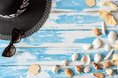 Hasır şapka ve güneş gözlüğü ile mavi ahşap tahta üzerinde deniz kabuklarını. Yaz tatil arka plan.