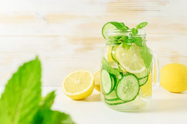 Detox water infused with sliced lemon, cucumber and sprigs of mint on wooden background.