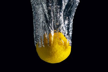 Siyah arka planda izole edilmiş su sıçramasında taze sarı limon. En az gıda konsepti.