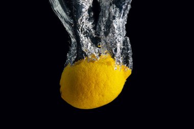 Siyah arka planda izole edilmiş su sıçramasında taze sarı limon. En az gıda konsepti.