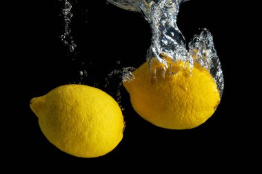 Siyah arka planda izole edilmiş su sıçramasında taze sarı limon. En az gıda konsepti.