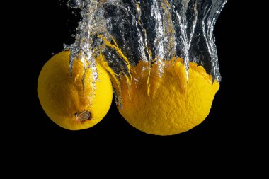 Siyah arka planda izole edilmiş su sıçramasında taze sarı limon. En az gıda konsepti.
