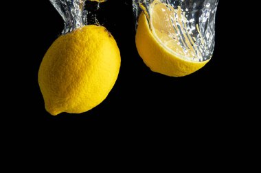 Siyah arka planda izole edilmiş su sıçramasında taze sarı limon. En az gıda konsepti.