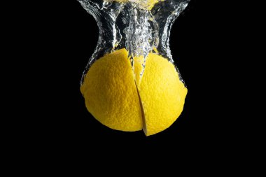 Siyah arka planda izole edilmiş su sıçramasında taze sarı limon. En az gıda konsepti.