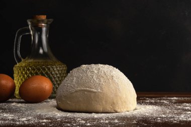 Ekmek ya da pizza için taze çiğ hamur. Koyu ahşap bir masada yumurta ve yağlı..
