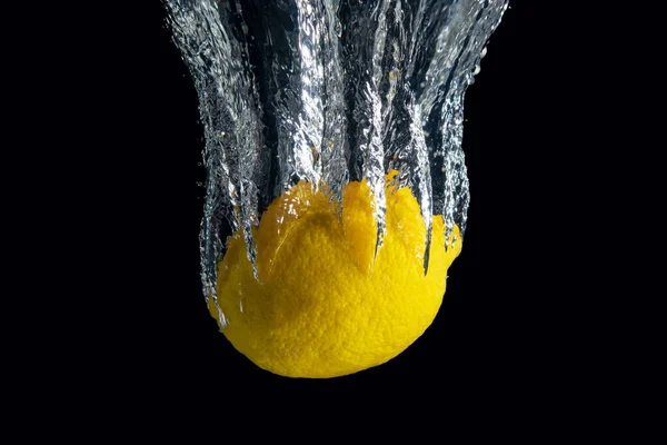 Siyah arka planda izole edilmiş su sıçramasında taze sarı limon. En az gıda konsepti.
