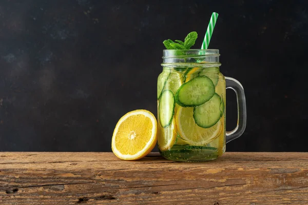 Detox water with sliced lemon and cucumber in a jar on dark background. Healthy concept.