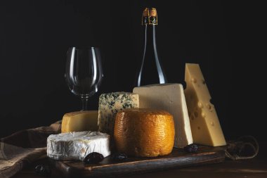 Kırsal ahşap masada bir bardak şarapla çeşitli peynir çeşitleri. Koyu arkaplan.