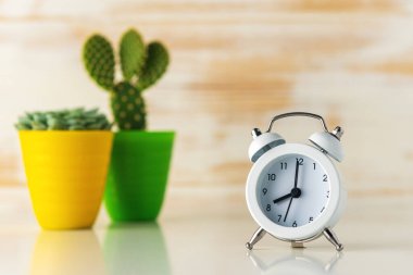 Tahta masadaki kaktüslü beyaz çalar saat. Asgari zaman kavramı.
