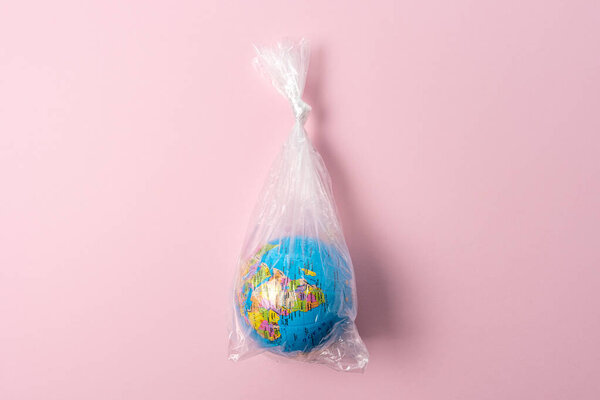 Earth globe in plastic bag on pink background. Minimal ecology concept.