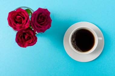 Kırmızı gül çiçeğinin yaratıcı bileşimi ve mavi arka planda bir fincan kahve. Asgari bahar kavramı.