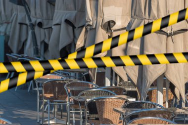 Bariyer bandı, karantina, tecrit konsepti, giriş yasağı. Geçmeyin. Güneş doğarken sokağın karşısındaki restoranda şemsiyeli boş masalar..