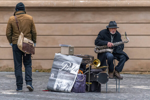 Прага, Чешская Республика - 19 января 2020 года: Старик, уличный музыкант с саксофоном, сидящий на улице
.