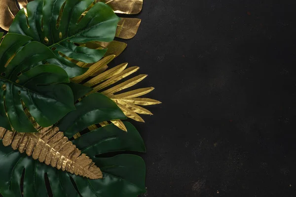 Creative layout with gold and green tropical palm leaves on black background. Minimal summer abstract pattern.