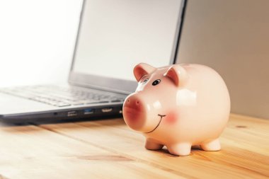 Domuz kumbarası ahşap bir masada dizüstü bilgisayarla. Para biriktirme kavramı.