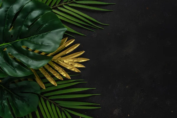 Creative layout with gold and green tropical palm leaves on black background. Minimal summer abstract pattern.