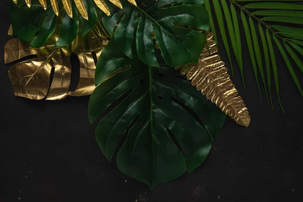 Creative layout with gold and green tropical palm leaves on black background. Minimal summer abstract pattern.