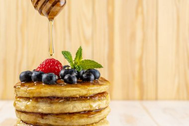 Taze böğürtlenli leziz krepler ve ahşap zemine bal damlatan. Yiyecek konsepti.