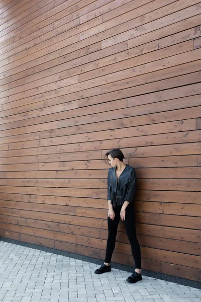 Chica en una chaqueta de cuero negro cerca de la pared de madera — Foto de Stock