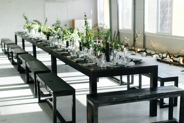 Stylish table, loft. Design room in the loft style. Black table, chairs, dishes, candles. Jars with greens.