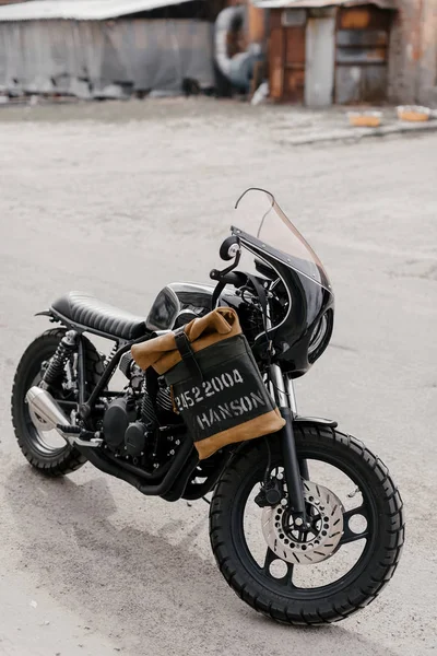 Skórzany plecak w pobliżu motocykla. Połowa czarny motocykl w garażu. Motocykl kaferacers. — Zdjęcie stockowe