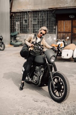 Onun motosiklet üzerinde oturan bir bayan. Motosiklet Garaj. Bir kadında bir deri ceket. Siyah motosiklet. Kısa saç kesimi olan bir kadın. Bisiklet