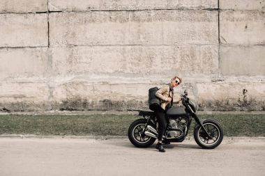 Onun motosiklet üzerinde oturan bir bayan. Gri bir duvara yakın motosiklet. Bir kız bir motosiklet sürmek. Kısa saçlı kız. Bisiklet