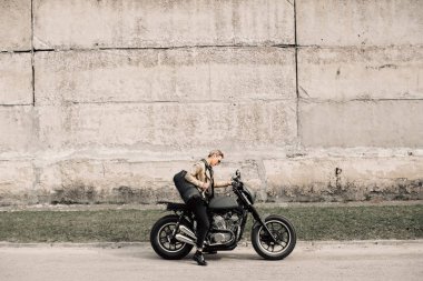 Onun motosiklet üzerinde oturan bir bayan. Gri bir duvara yakın motosiklet. Bir kız bir motosiklet sürmek. Kısa saçlı kız. Bisiklet