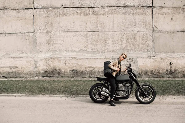 Mujer sentada en su motocicleta. Moto cerca de una pared gris. Una chica monta una motocicleta. La chica con el pelo corto. Moto —  Fotos de Stock