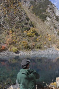 Yeşil ceketli adamı göl kenarında oturur