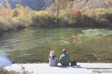 Renkli sonbahar ahşap tarafından çevrili gölün oturan bir çift