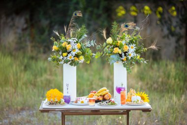 Beyaz ahşap bir masada çiçekler, kokteyller ve abur cuburlarla süslenmiş bir açık büfe.