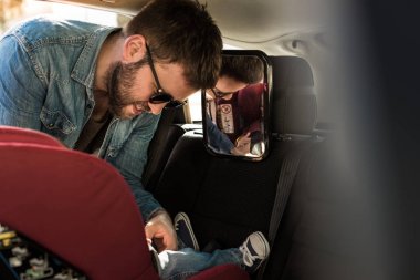 Father fasten his baby in car seat clipart