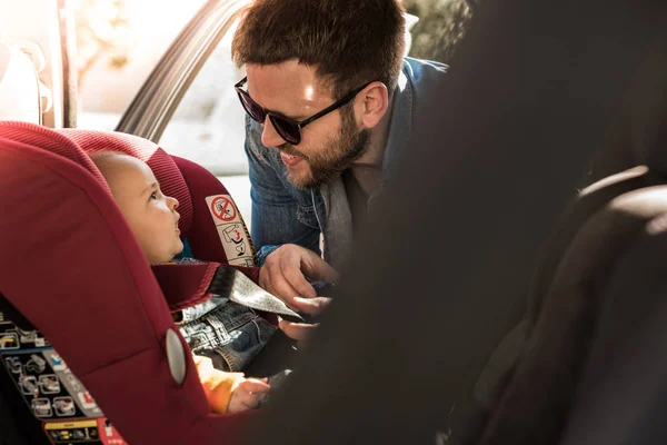 Pai prenda seu bebê no assento do carro — Fotografia de Stock