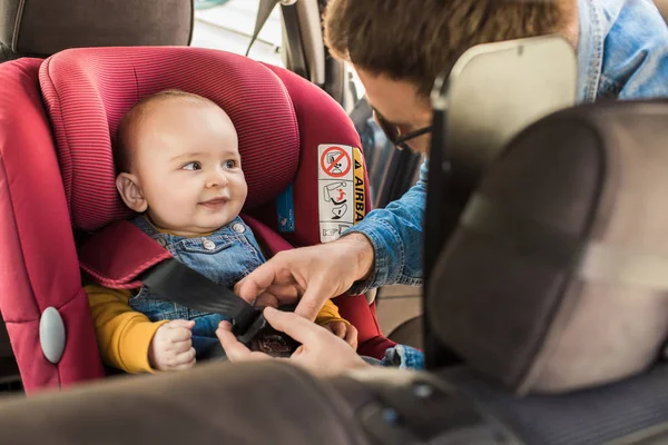 Pai prenda seu bebê no assento do carro — Fotografia de Stock