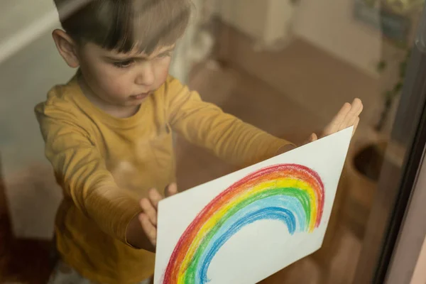 有灵感的小男孩抱着彩虹的图画穿过窗户 — 图库照片