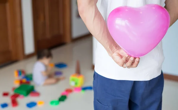 Pai escondendo um balão de coração rosa nas costas, animado para surpreender sua filha para o seu aniversário — Fotografia de Stock