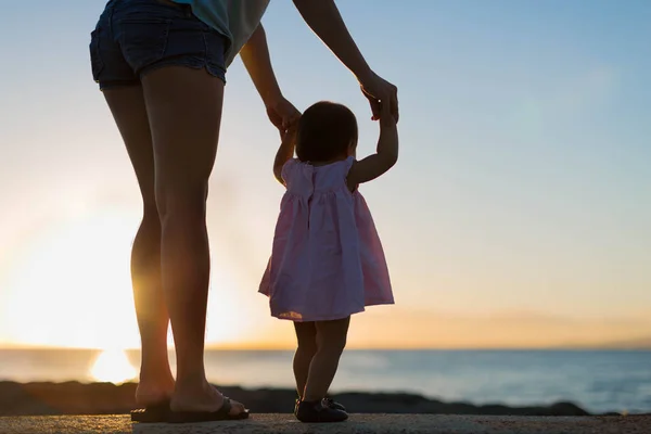 Мати і дочка тримаються за руки, спостерігаючи за заходом сонця разом на пляжі . — стокове фото