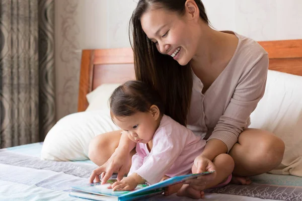 Lindo asiático niño siendo leído a por su joven madre . — Foto de Stock